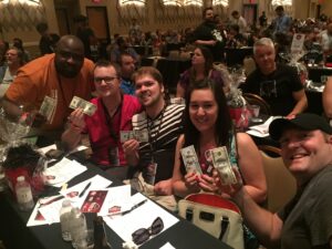 A group of people at a trivia tournament holding up $100 bills while smiling.